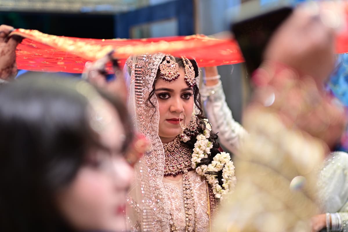 Wedding Photography - Beautiful bride walking into the wedding hall with family members holding a dupatta over her head